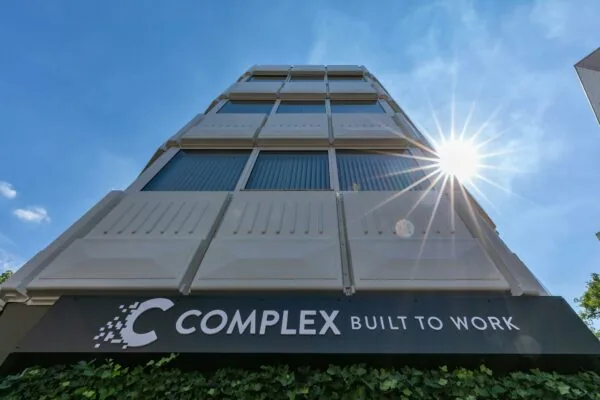 Vooraanzicht van het moderne kantoorgebouw COMPLEX aan de 1e Hogeweg, met de zon die schijnt aan een heldere blauwe lucht.